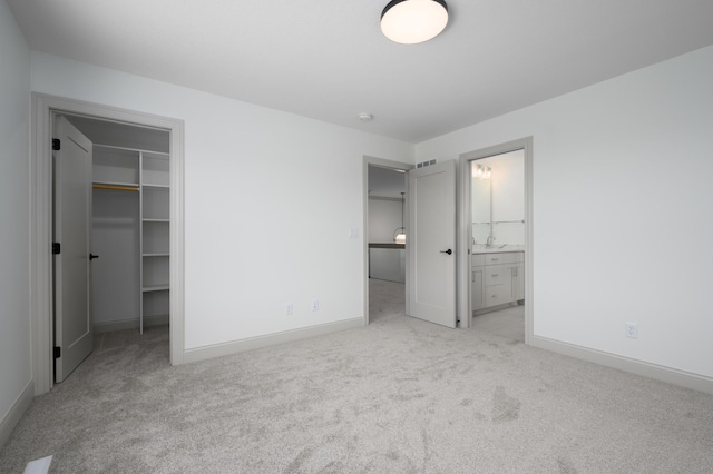 unfurnished bedroom featuring a closet, a spacious closet, ensuite bath, and light carpet