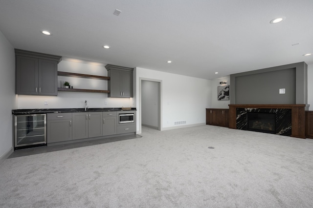 kitchen featuring gray cabinets, stainless steel microwave, wine cooler, light colored carpet, and a premium fireplace