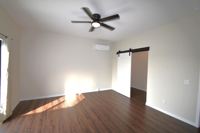 empty room featuring dark wood-type flooring, a wall unit AC, a barn door, and ceiling fan