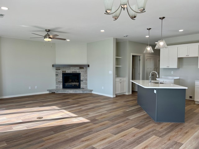 kitchen featuring a kitchen island with sink, hanging light fixtures, light wood-type flooring, white cabinets, and a fireplace