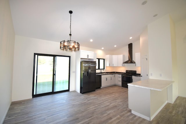 kitchen with white cabinets, dark hardwood / wood-style flooring, black appliances, decorative light fixtures, and wall chimney range hood