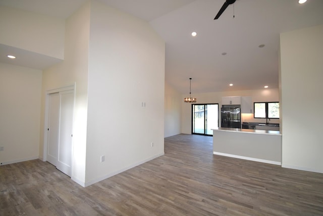 unfurnished living room featuring ceiling fan with notable chandelier, dark hardwood / wood-style floors, sink, and high vaulted ceiling