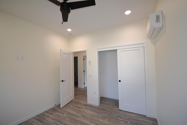 unfurnished bedroom featuring light hardwood / wood-style flooring, a closet, a wall unit AC, and ceiling fan