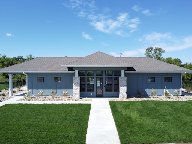 rear view of house featuring roof with shingles, board and batten siding, and a yard