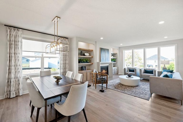 dining room featuring light wood finished floors, baseboards, built in features, and a glass covered fireplace