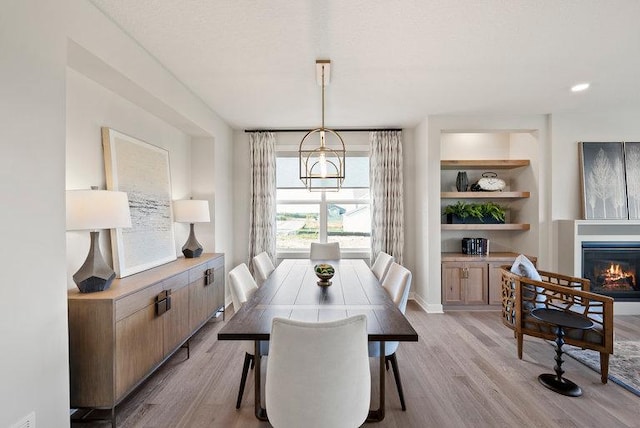 dining room with built in features, a glass covered fireplace, baseboards, and light wood finished floors