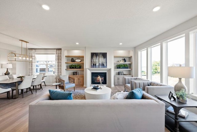 living room with a textured ceiling, light wood finished floors, and a glass covered fireplace