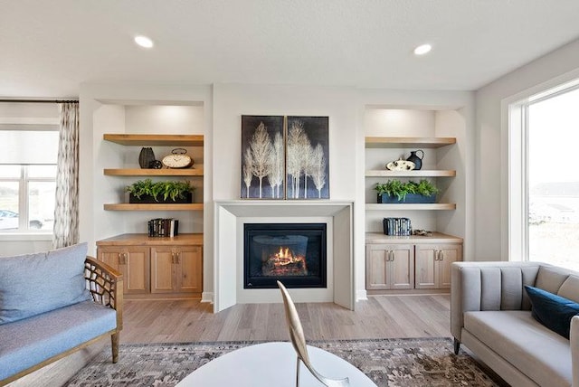 living room featuring built in shelves, plenty of natural light, and light wood-style flooring