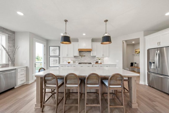 kitchen with custom exhaust hood, stainless steel appliances, light countertops, light wood-type flooring, and backsplash