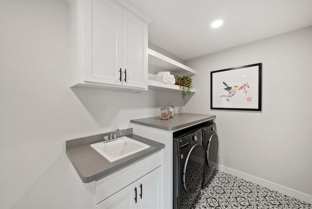 laundry room featuring washing machine and dryer, cabinet space, a sink, and baseboards