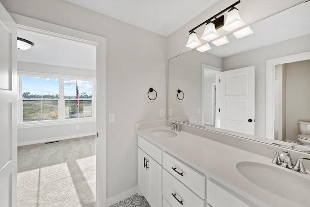 full bathroom featuring double vanity, a sink, toilet, and baseboards