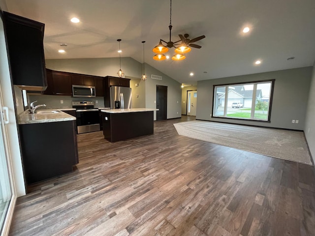 kitchen with appliances with stainless steel finishes, vaulted ceiling, a kitchen island, wood-type flooring, and sink