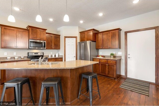 kitchen with decorative light fixtures, dark hardwood / wood-style floors, light stone counters, and stainless steel appliances