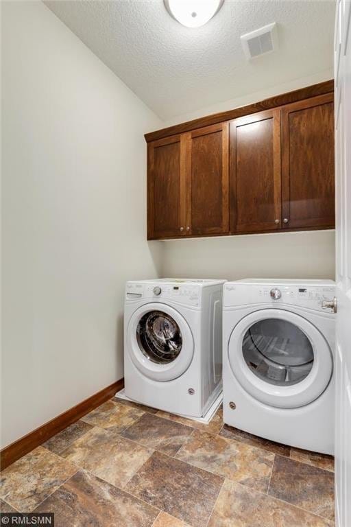 clothes washing area with dark tile flooring, independent washer and dryer, a textured ceiling, and cabinets