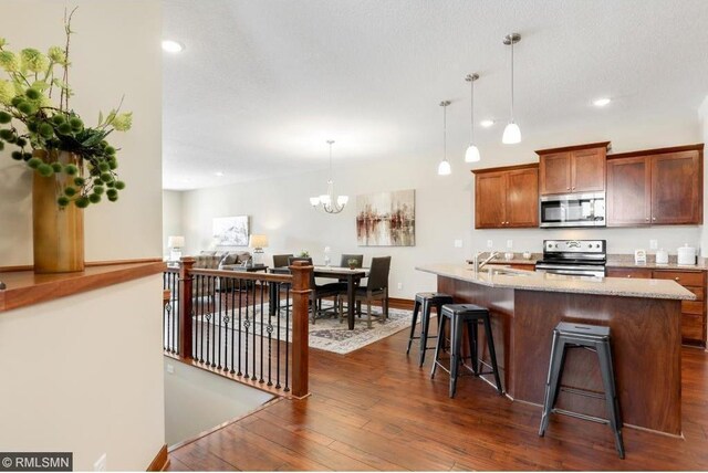 kitchen featuring a notable chandelier, decorative light fixtures, dark wood-type flooring, appliances with stainless steel finishes, and light stone counters