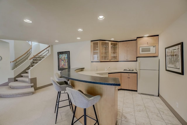 kitchen with a kitchen breakfast bar, white appliances, kitchen peninsula, and light brown cabinetry