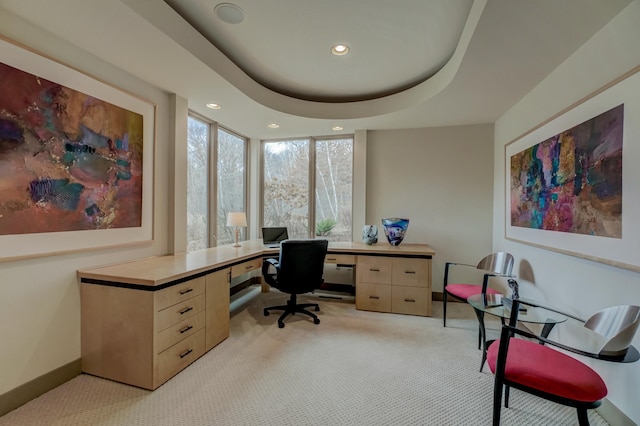 home office with expansive windows, light colored carpet, and a tray ceiling