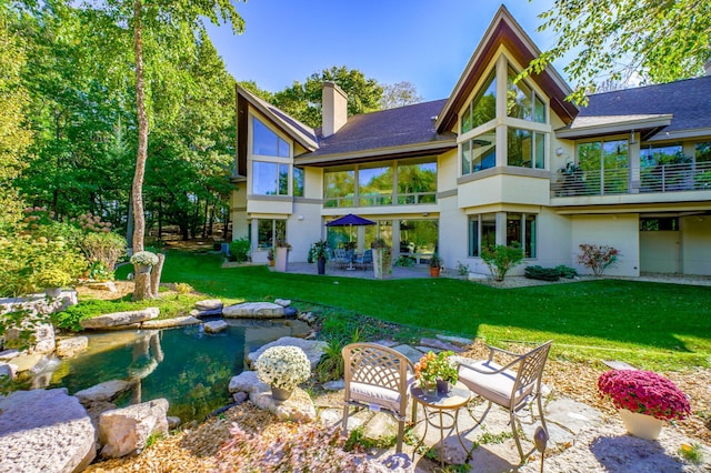 rear view of property featuring a lawn, a balcony, and a patio