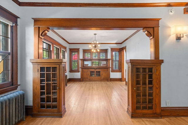 unfurnished dining area featuring radiator heating unit, a chandelier, light wood-type flooring, and crown molding