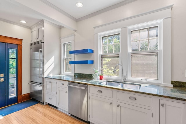 kitchen with dark stone countertops, appliances with stainless steel finishes, light wood-type flooring, sink, and white cabinetry