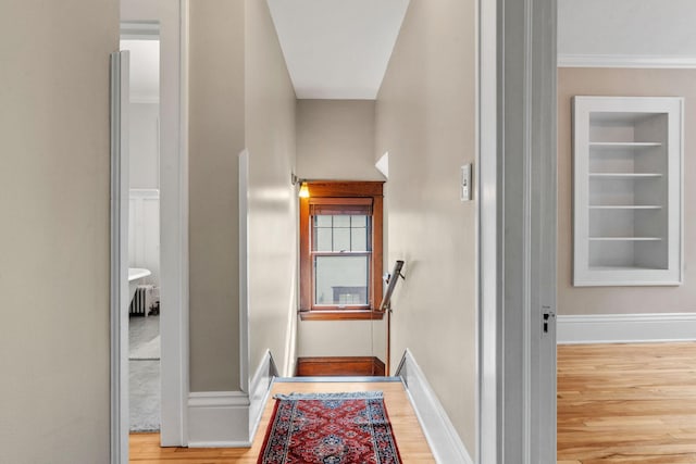 hall featuring radiator heating unit, light wood-type flooring, built in shelves, and crown molding