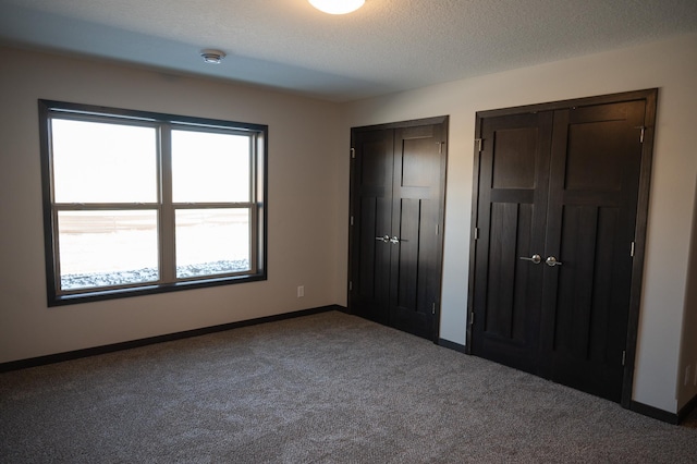 unfurnished bedroom featuring carpet flooring, two closets, and a textured ceiling