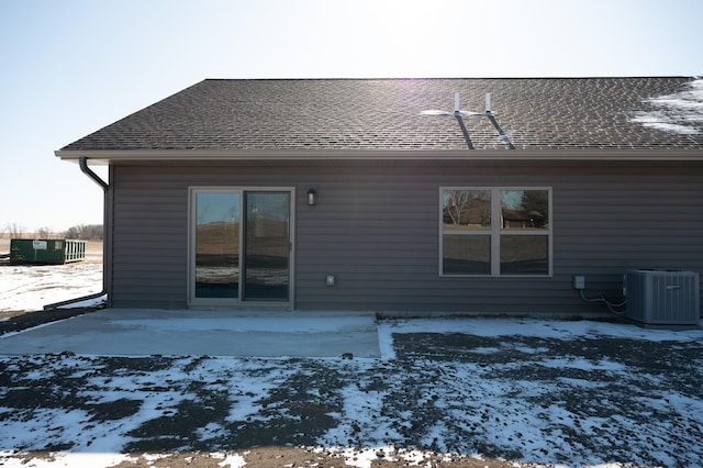 snow covered back of property with cooling unit and a patio