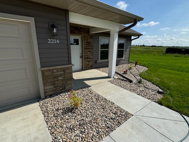 2214 Red Bird Ln, Fairmont, MN 56031 - view of exterior entry with stone siding, an attached garage, and a yard