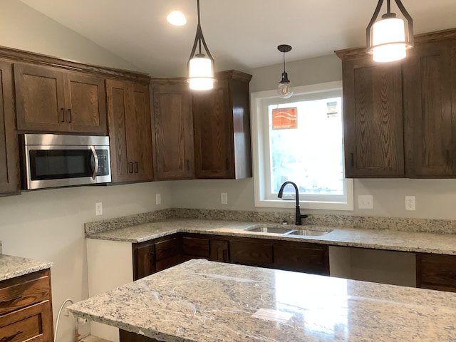 kitchen featuring hanging light fixtures, lofted ceiling, sink, and light stone countertops