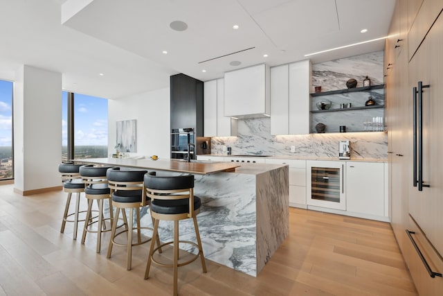 bar featuring decorative backsplash, white cabinets, beverage cooler, cooktop, and light hardwood / wood-style flooring