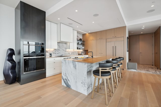 kitchen with tasteful backsplash, a kitchen bar, light hardwood / wood-style floors, white cabinets, and a kitchen island with sink