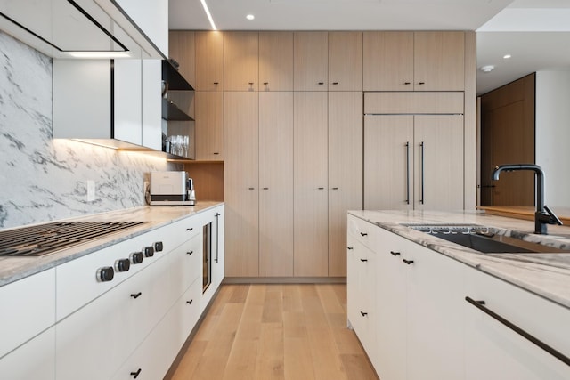 kitchen with white cabinets, backsplash, light wood-type flooring, sink, and light stone counters