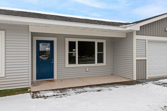 snow covered property entrance with a garage