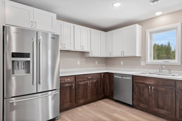 kitchen with white cabinets, dark brown cabinetry, sink, light wood-type flooring, and appliances with stainless steel finishes