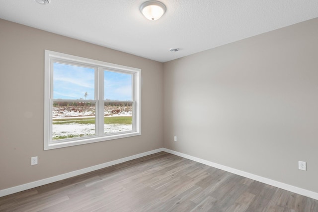 spare room with light wood-type flooring, a textured ceiling, and plenty of natural light