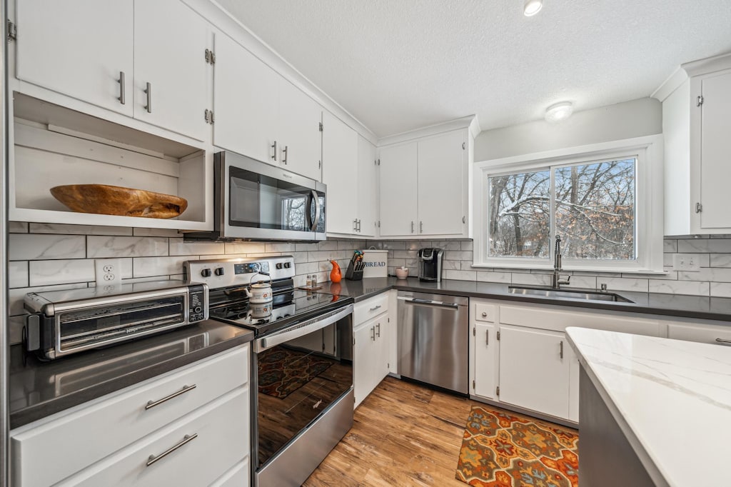 kitchen featuring sink, white cabinetry, stainless steel appliances, light hardwood / wood-style floors, and decorative backsplash