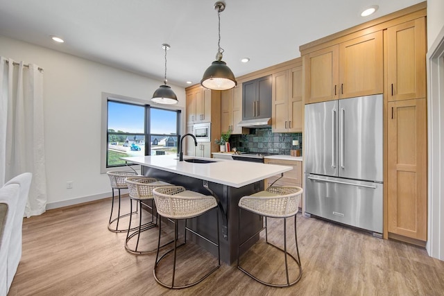 kitchen with hanging light fixtures, an island with sink, stainless steel appliances, sink, and light hardwood / wood-style flooring