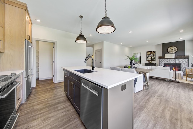 kitchen featuring light brown cabinets, a tiled fireplace, a center island with sink, light wood-type flooring, and sink