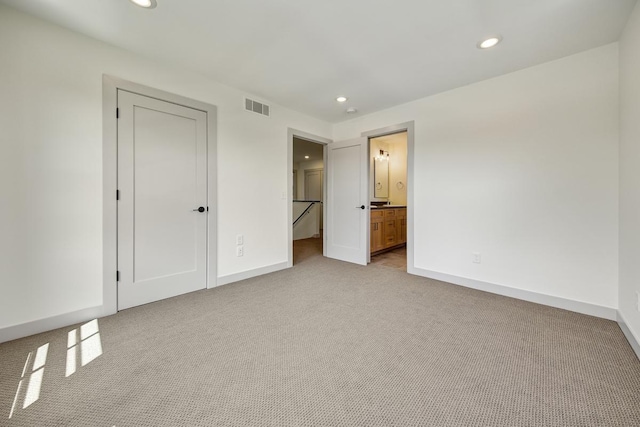 unfurnished bedroom with light carpet, ensuite bath, and a closet