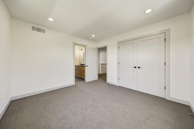 unfurnished bedroom featuring a closet, dark colored carpet, and ensuite bathroom