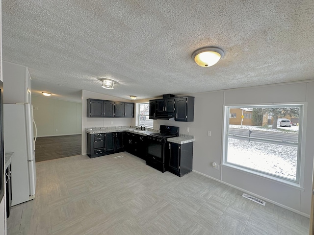 kitchen with electric range, a healthy amount of sunlight, a textured ceiling, and white fridge