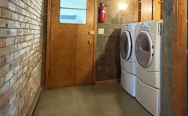 laundry area with cabinets, dark tile flooring, washing machine and clothes dryer, and brick wall