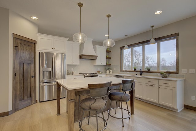 kitchen featuring light wood-type flooring, a center island, white cabinets, stainless steel appliances, and premium range hood