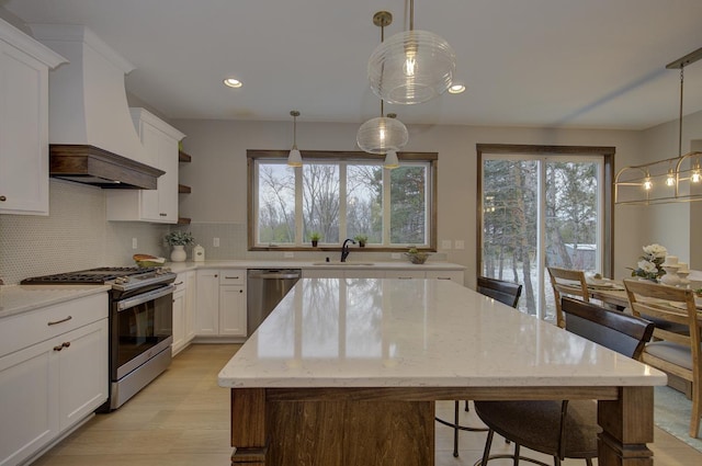 kitchen featuring decorative light fixtures, appliances with stainless steel finishes, custom range hood, and sink