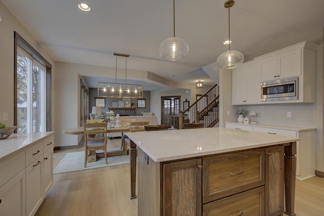 kitchen with a center island, light hardwood / wood-style flooring, stainless steel microwave, and white cabinetry