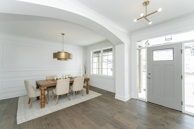 foyer with arched walkways, an inviting chandelier, dark wood finished floors, and crown molding