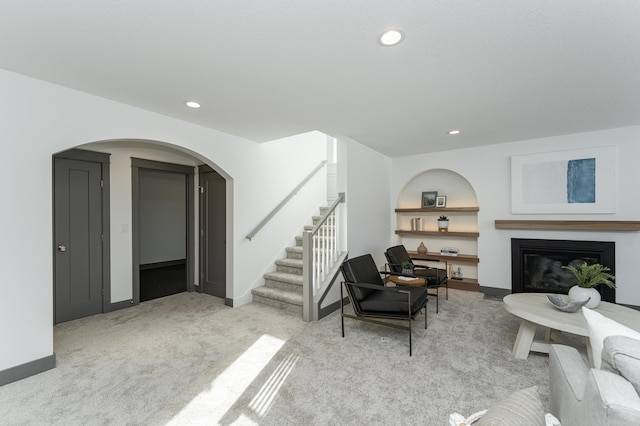 living area with arched walkways, recessed lighting, light colored carpet, stairway, and a glass covered fireplace