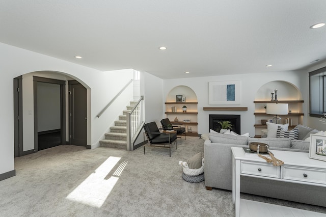 living area with arched walkways, light colored carpet, a fireplace, built in features, and stairs