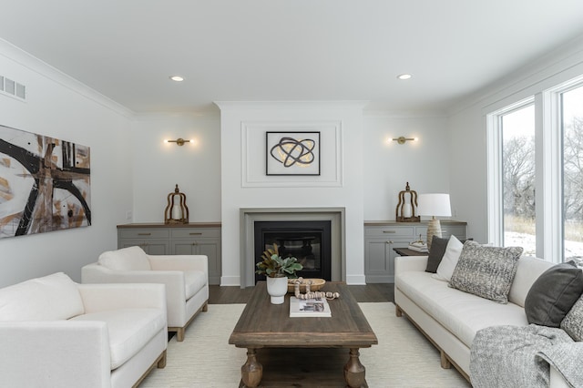 living area with recessed lighting, visible vents, light wood-type flooring, a glass covered fireplace, and crown molding