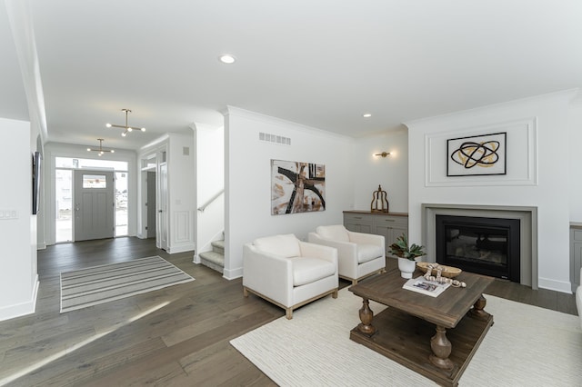 living area with visible vents, dark wood finished floors, a glass covered fireplace, stairway, and crown molding